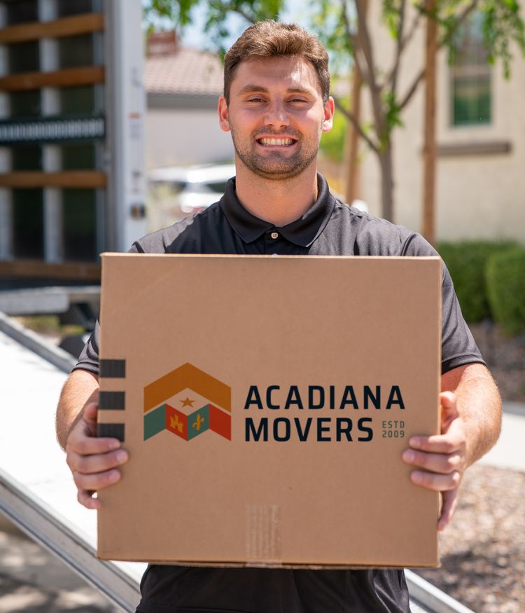 Mover holding Acadiana Movers box outside truck.