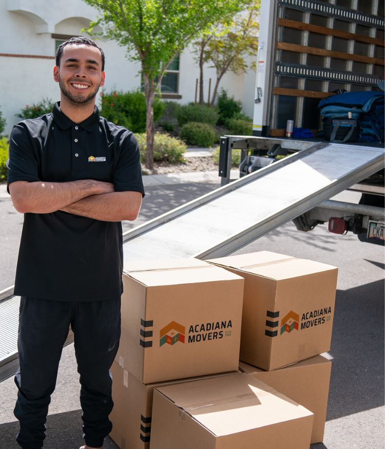 Smiling mover with boxes beside a truck ramp.