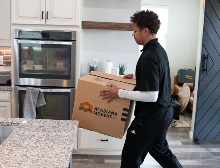 Person carrying moving box in kitchen.