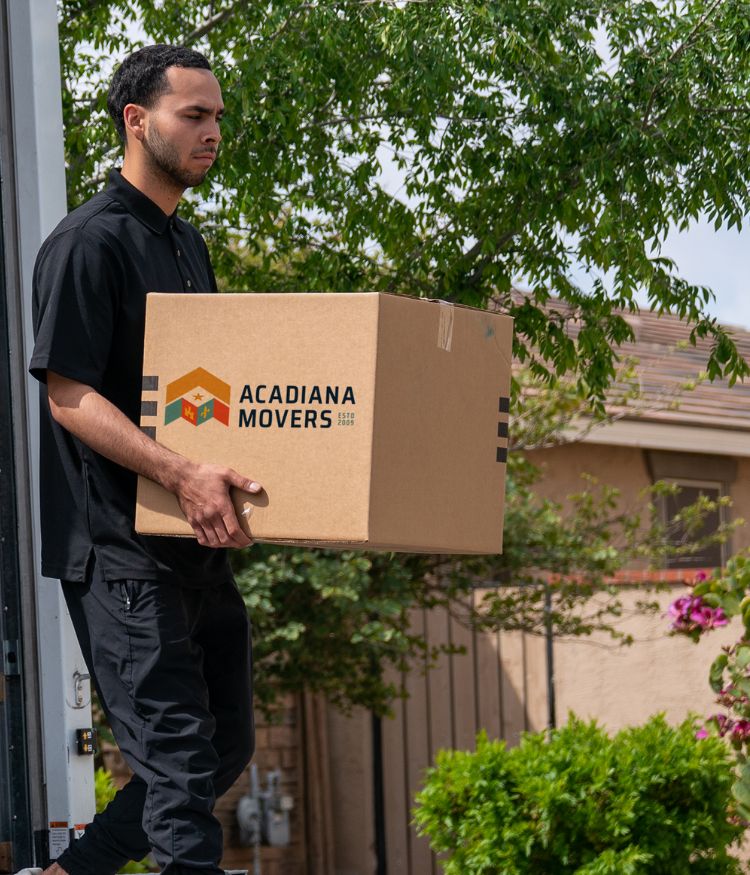 Mover carrying Acadiana Movers box outside.